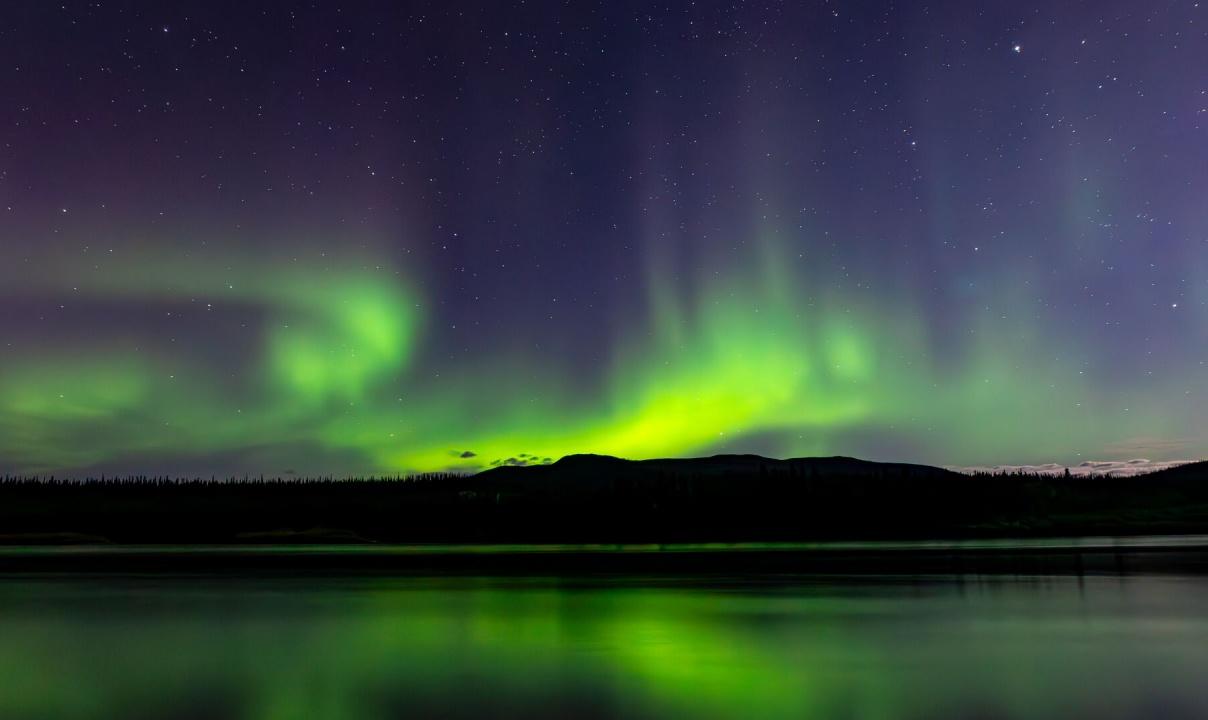 The green aurora lighting up the sky above a lake at night.
