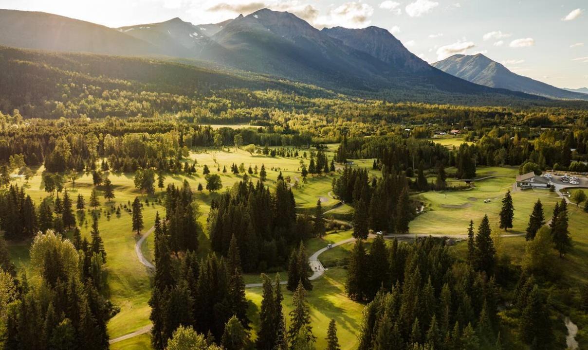 A golf course surrounded by forest and mountains.