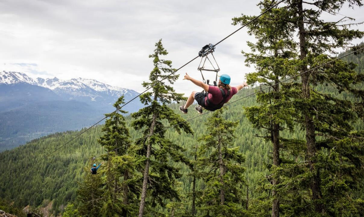 A person ziplining through the forest with snow-capped mountains in the background in Whistler, BC.
