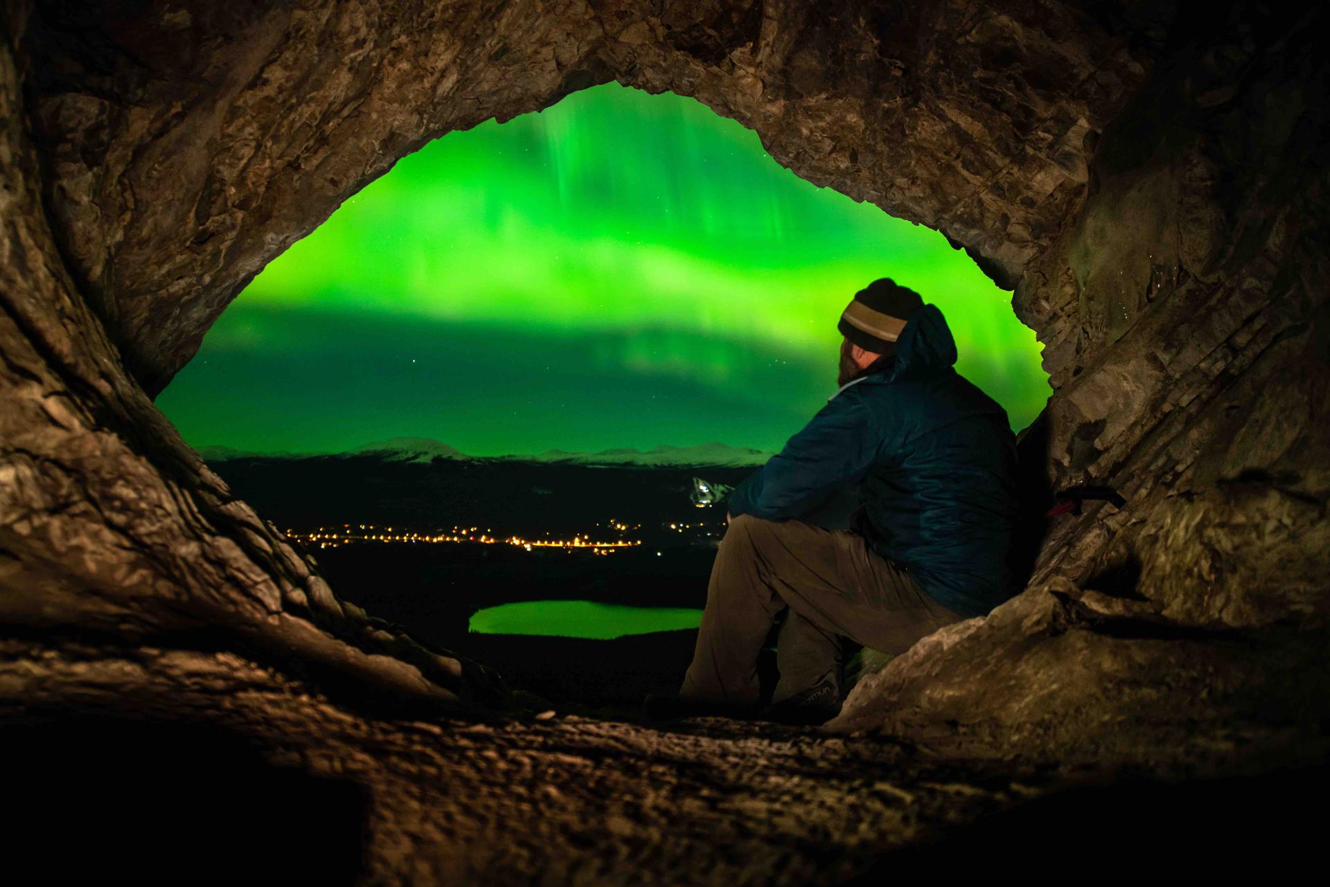 A man observing the Northern Lights in Yukon from the mouth of a cave