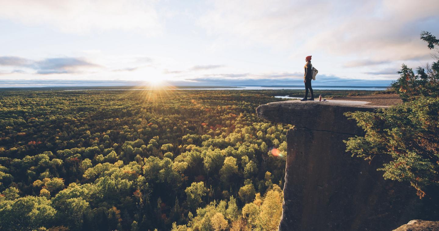 A hiker looks down at a river from a hill crest