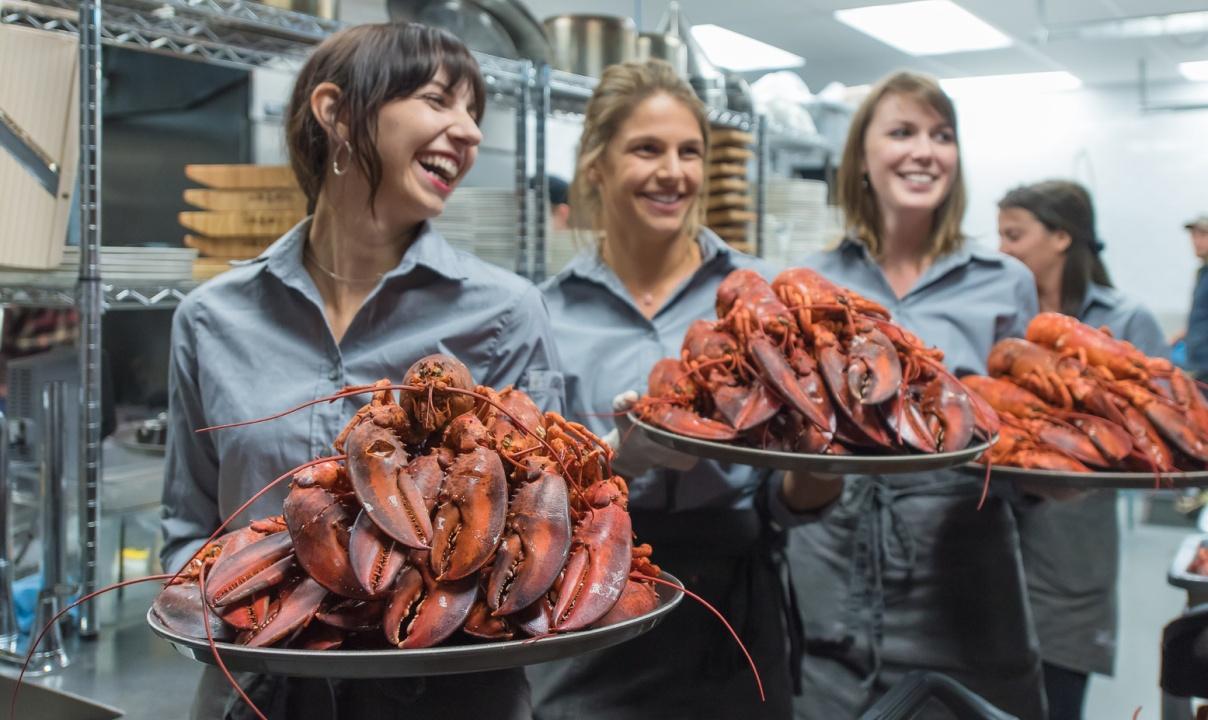 Three people holding plates of stacked fresh lobsters