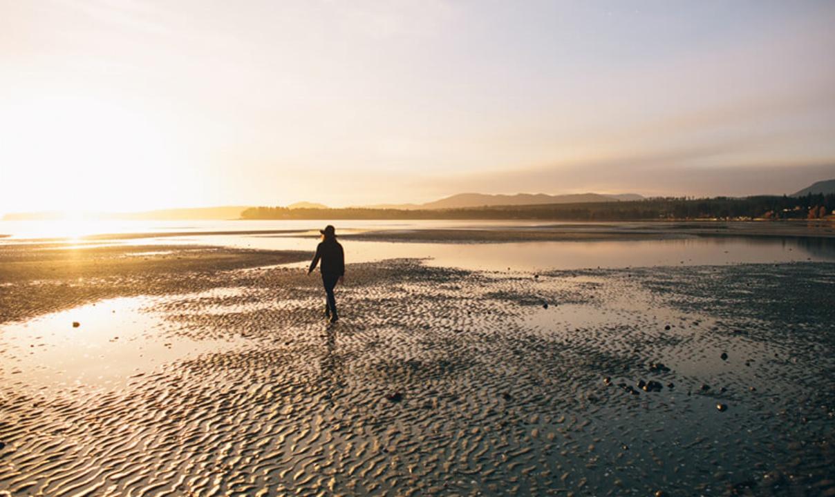 A person walking on a beach at low tide as the sun sets.