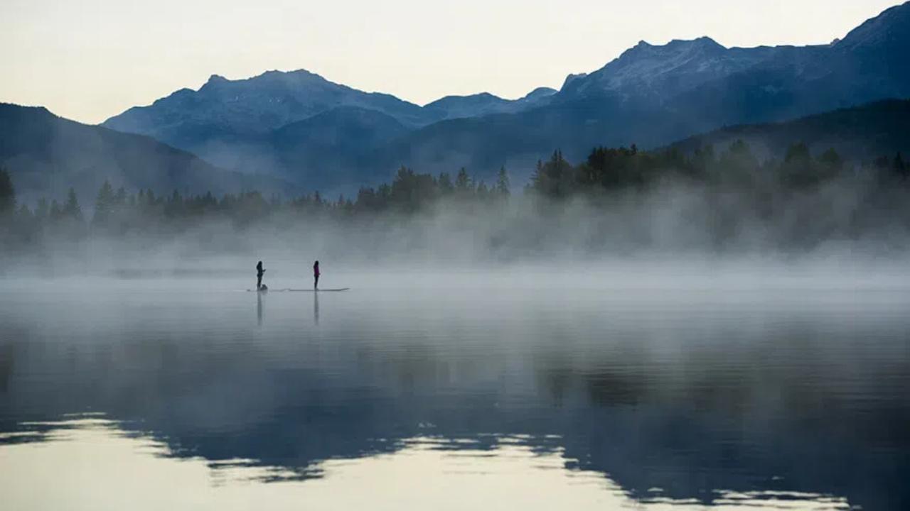 Two people paddle boarding on a misty mountain lake.