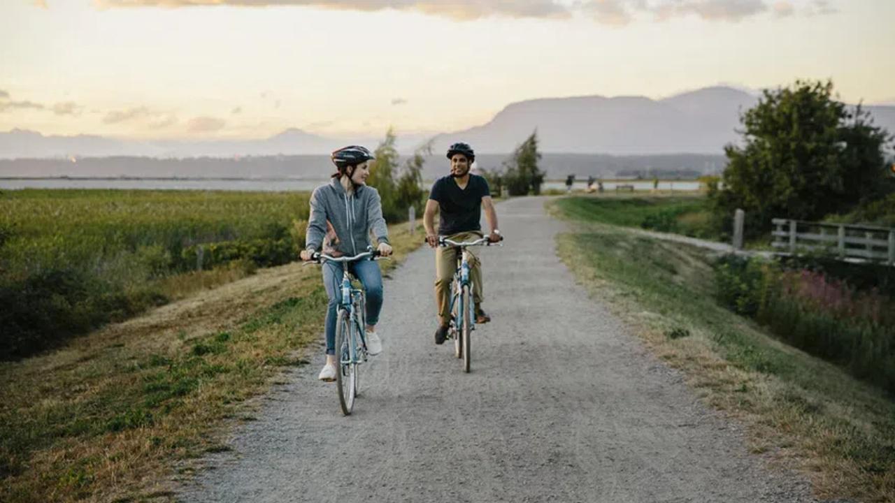 A man and a woman riding bicycles on the Dyke Trail in Richmond, BC.