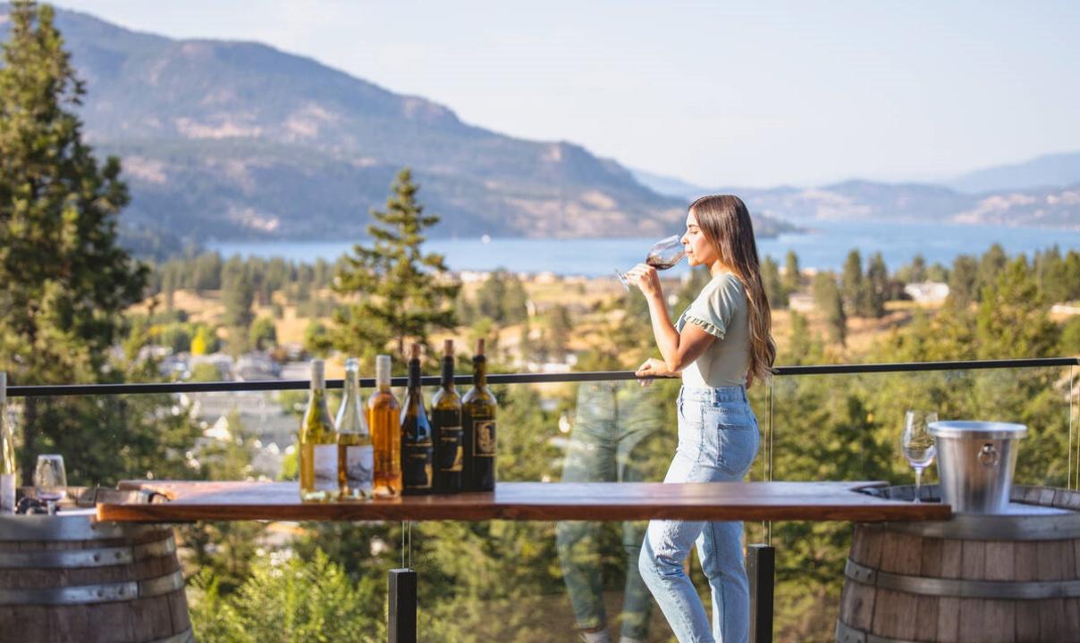 A young woman tasting wine on a deck overlooking a lake in the Okanagan.