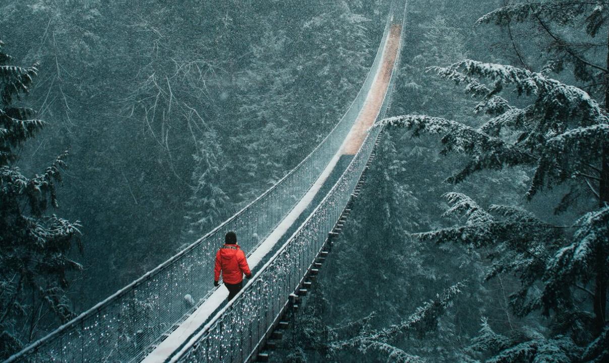 A person in a red coat walking across the Capilano Suspension Bridge.