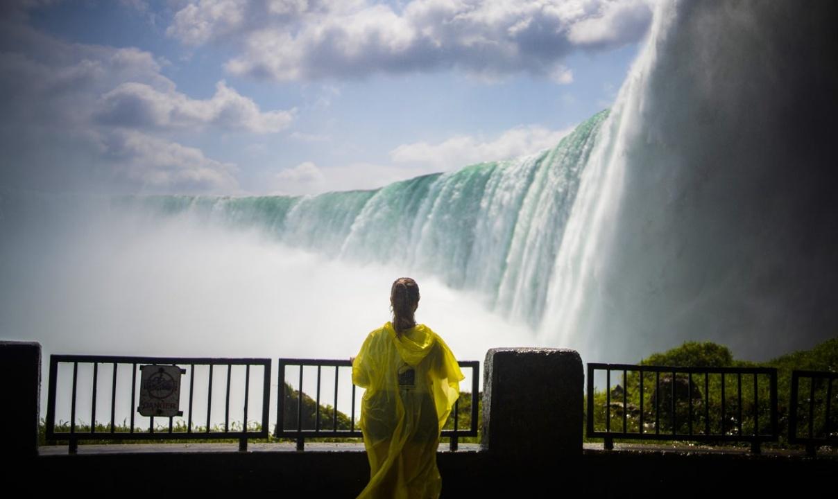 A woman in a yellow rain poncho observing Niagara Falls from a viewpoint below the top of the falls.