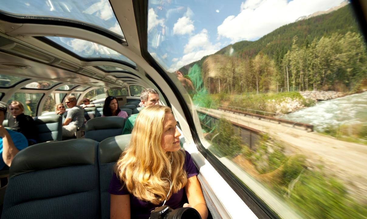 A woman looking out the window of an observation dome train car at the passing forest scenery.