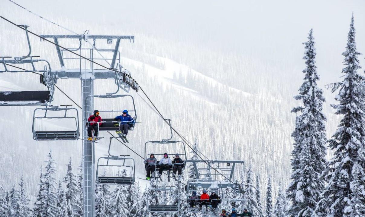 People riding a chairlift past snow-covered trees.