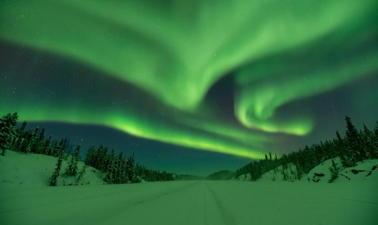 A snowy road with a green aurora overhead.