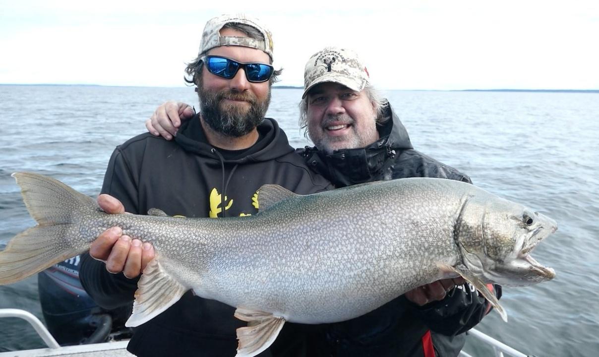 Two men standing on a boat deck showing off a large fish.