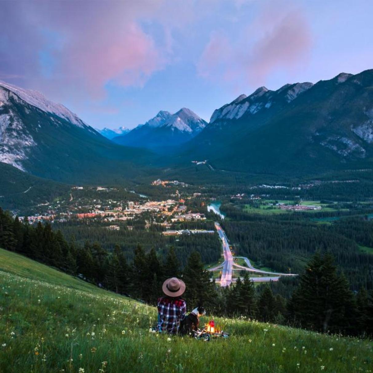 A woman sits in a meadow in view of the Rocky Mountains