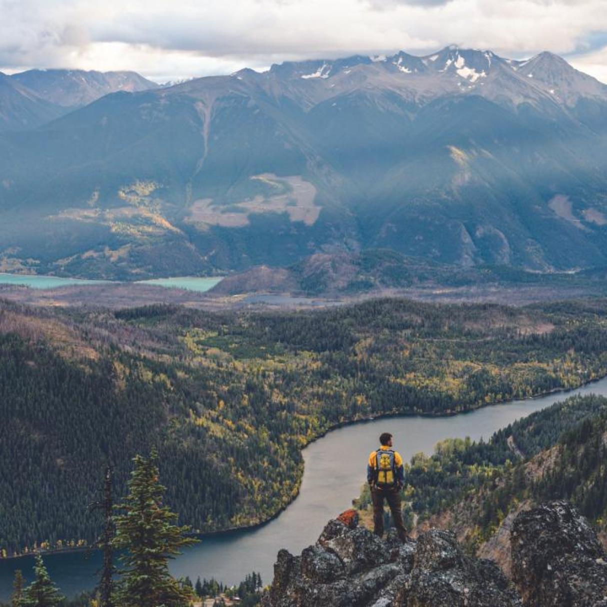 A hiker looks down at a river from a hill crest