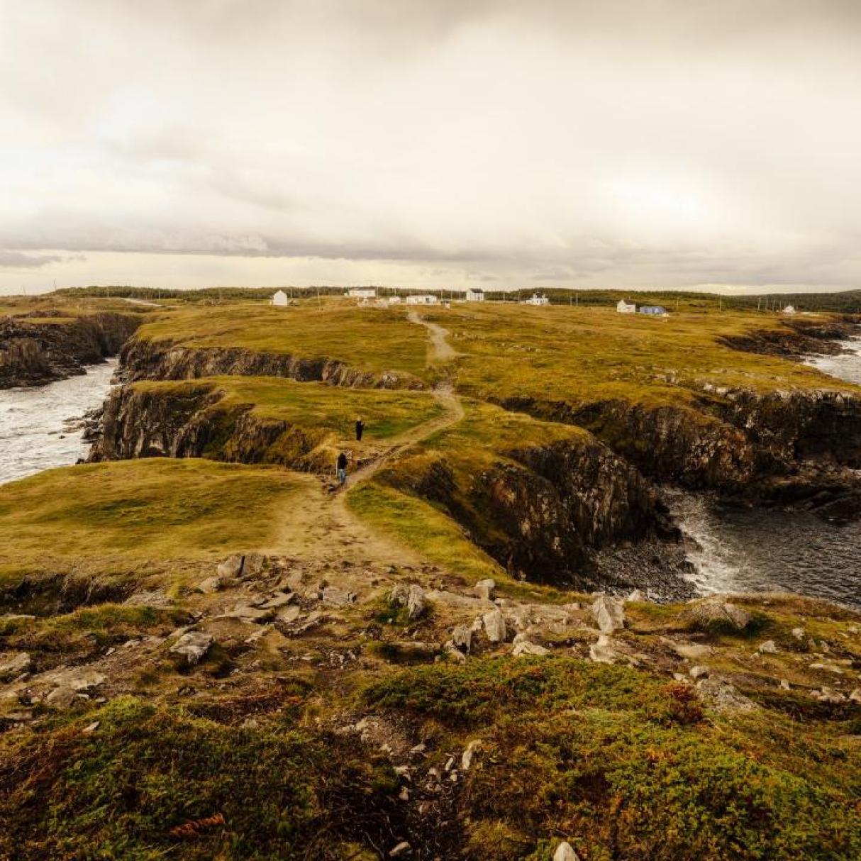 Two hikers walk along rugged cliffs with ocean on either side