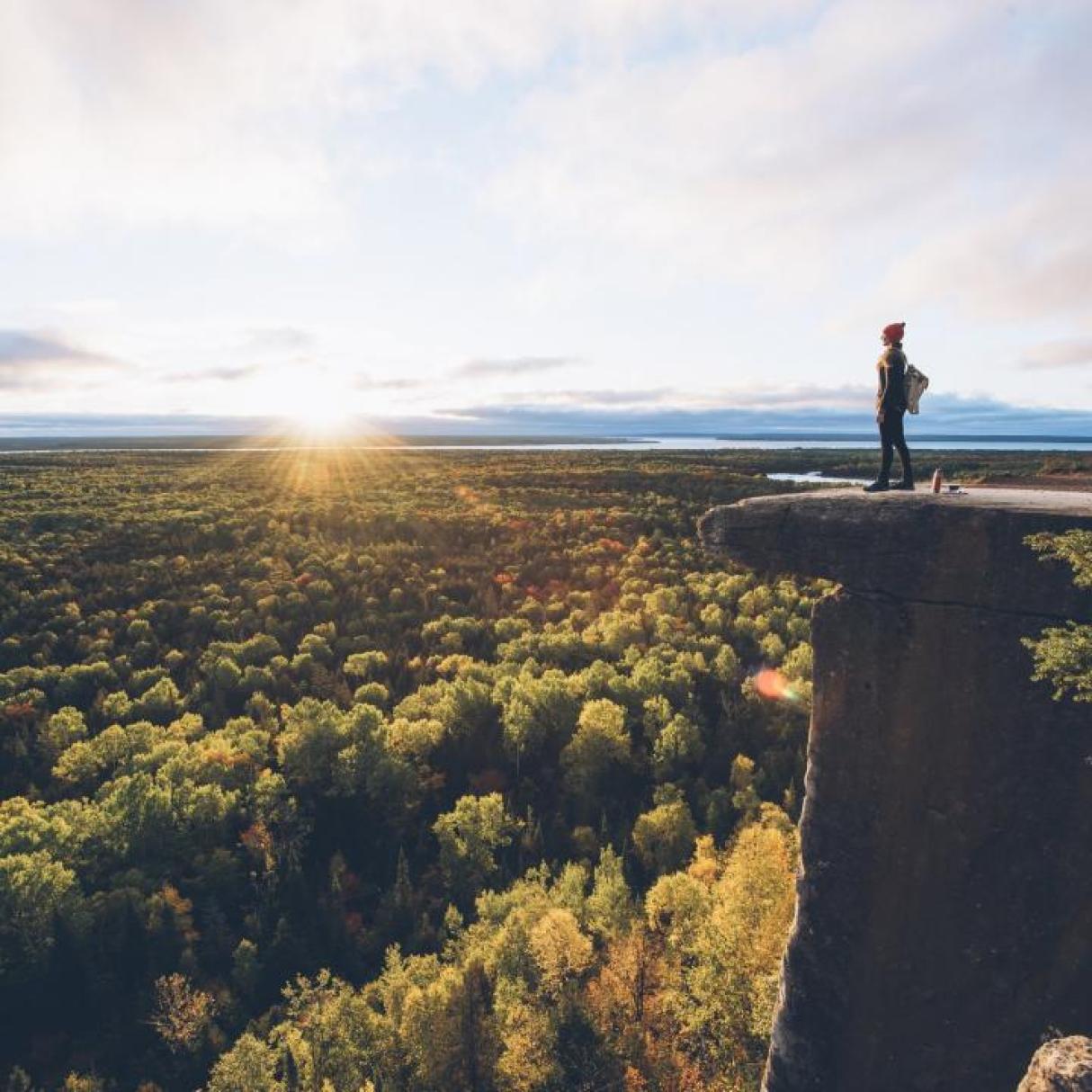 A person looking out on a lush green valley from a high ridge