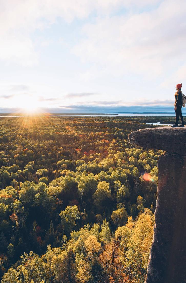 A person stands on a ridge with the sun on the horizon