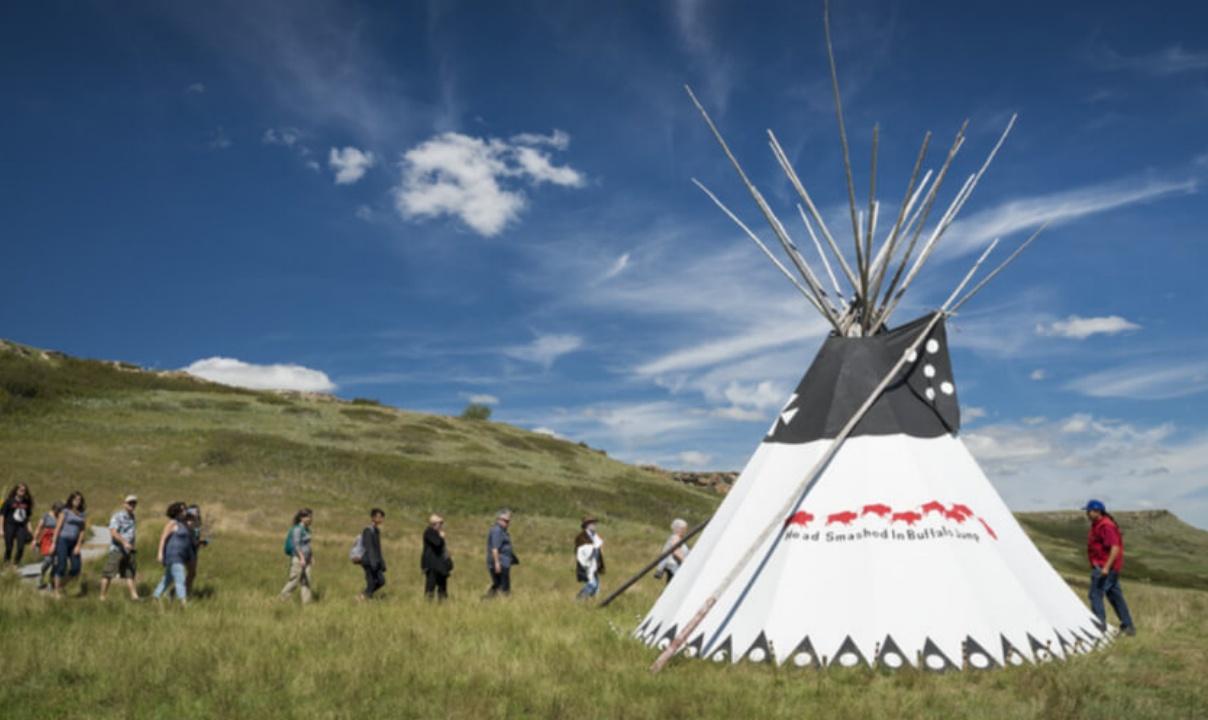 A group of people walking towards a teepee.