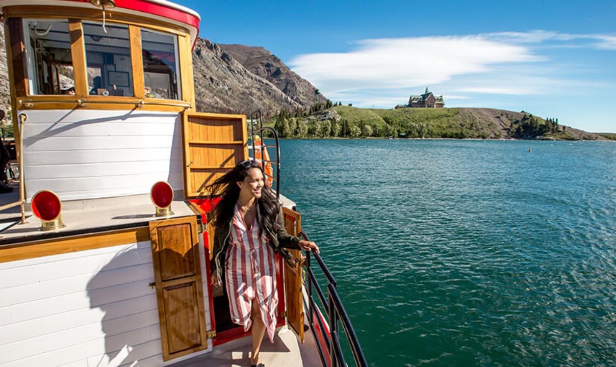 A woman stepping out of a cabin onto the deck of a boat on a lake.