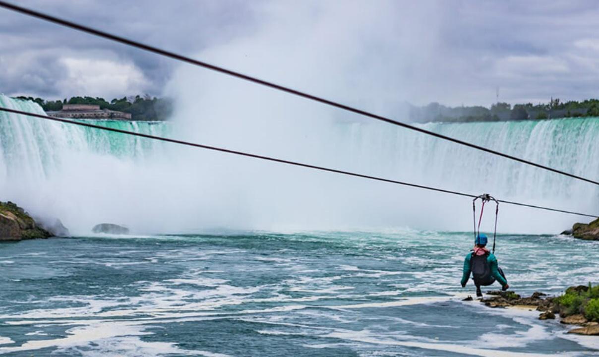 A person riding a zipline in front of Niagara Falls.