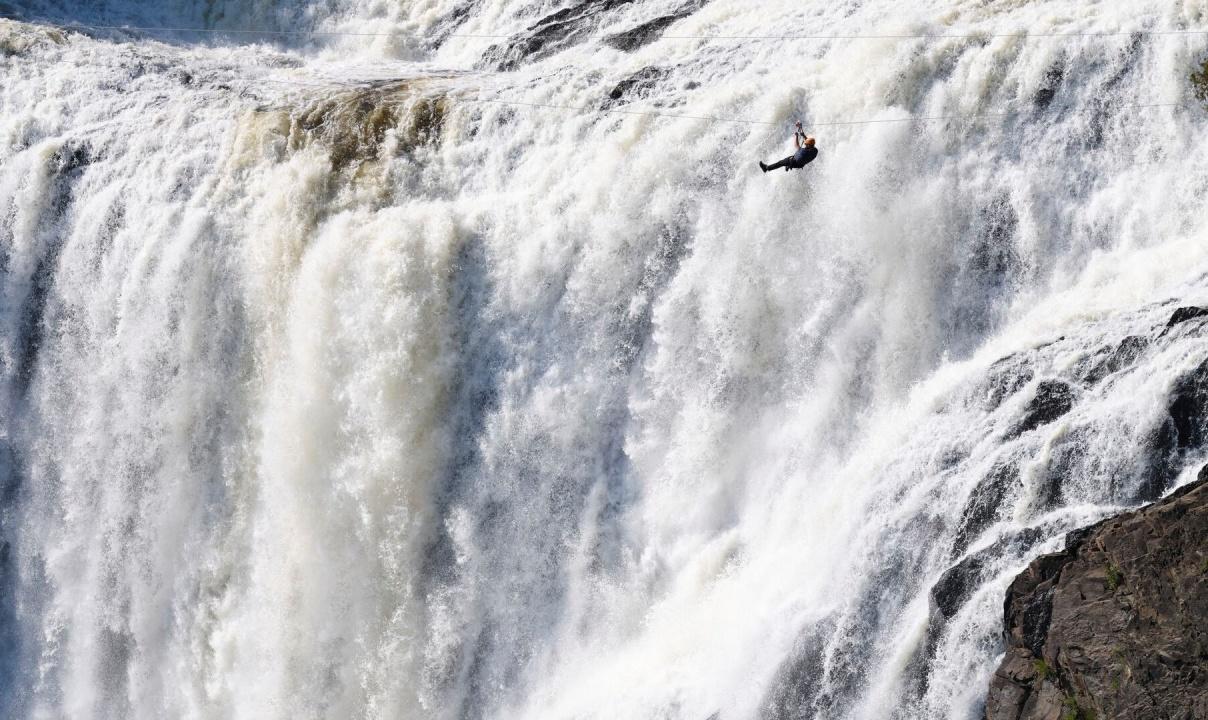 A person in silhouette ziplining in front of a large waterfall.