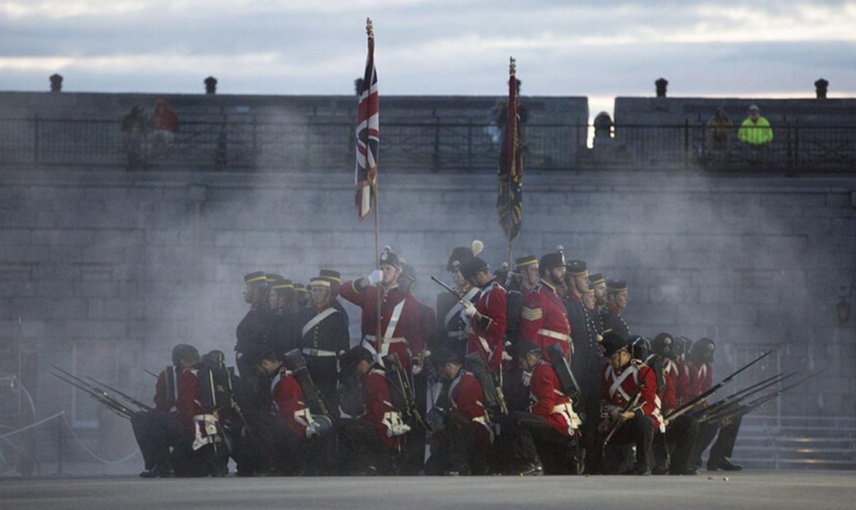 A group of people dressed in 19th century military uniforms reenacting a battle scene at Fort Henry in Ontario.