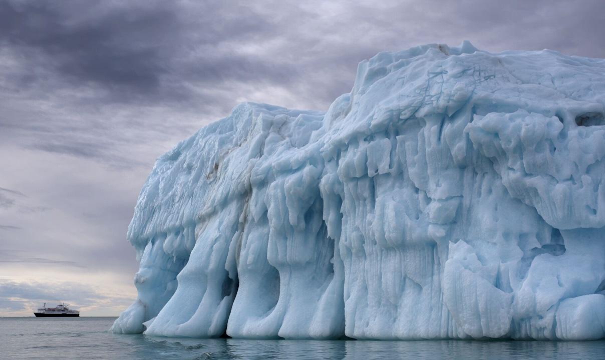 A large iceberg with a boat behind it in the distance.