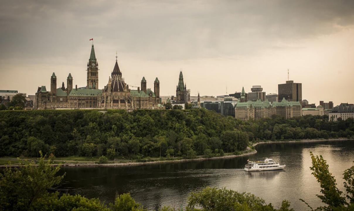 A view of the Parliament buildings in Ottawa with a river in the foreground.