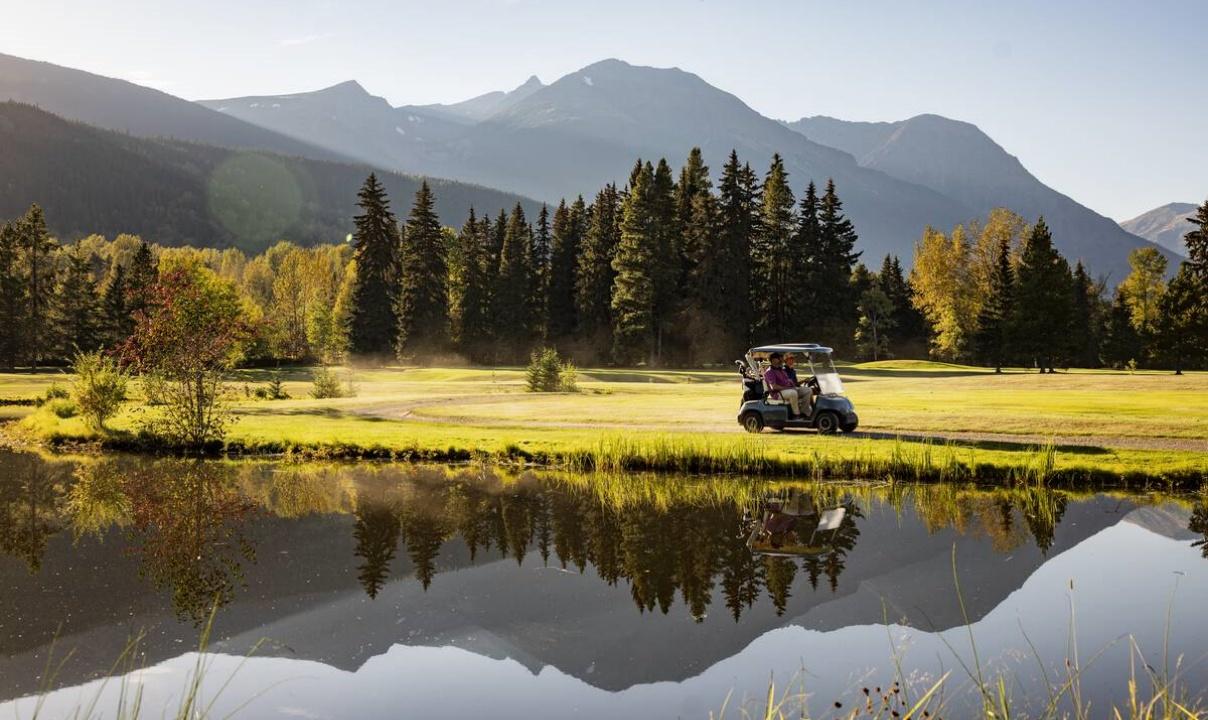 A golf cart driving on a golf course with trees and tall mountains in the background.