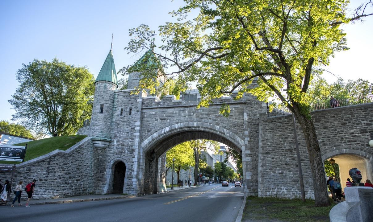 A stone archway with crenellations and a turret leading into the Fortifications of Quebec National Historic Site.